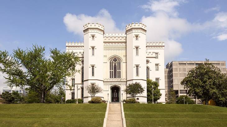 A white castle-like structure next to grass and trees under a blue sky with clouds