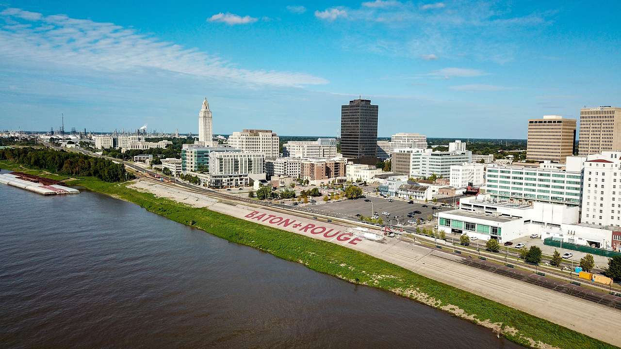 A river next to grass, a "Baton Rouge" sign, and city buildings
