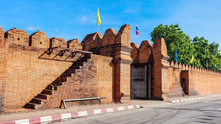 An old gate and wall made of bricks with flags on top as seen from the street An old gate and wall made of bricks with flags on top as seen from the street