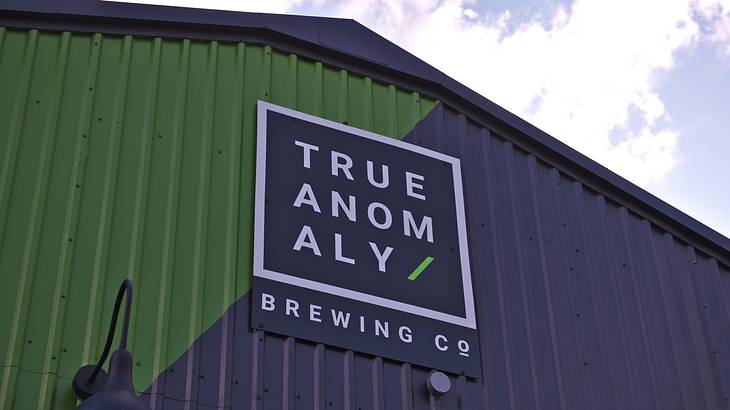 A green and blue building with a sign stating "True Anomaly Brewing Co" A green and blue building with a sign stating "True Anomaly Brewing Co"