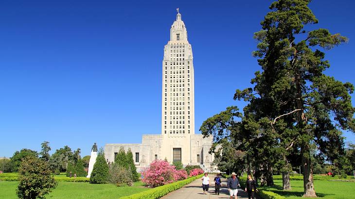 A tall white tower structure next to a garden and a walking path under a blue sky