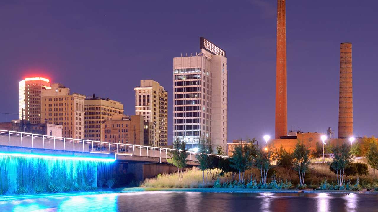 A river with an illuminated waterfall next to columns and buildings at night