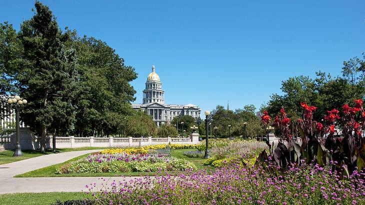 A flower garden and trees next to a large white stone building with a dome
