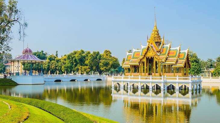 A gold-coloured palace in the middle of a pond with green lawns and trees surrounding A gold-coloured palace in the middle of a pond with green lawns and trees surrounding