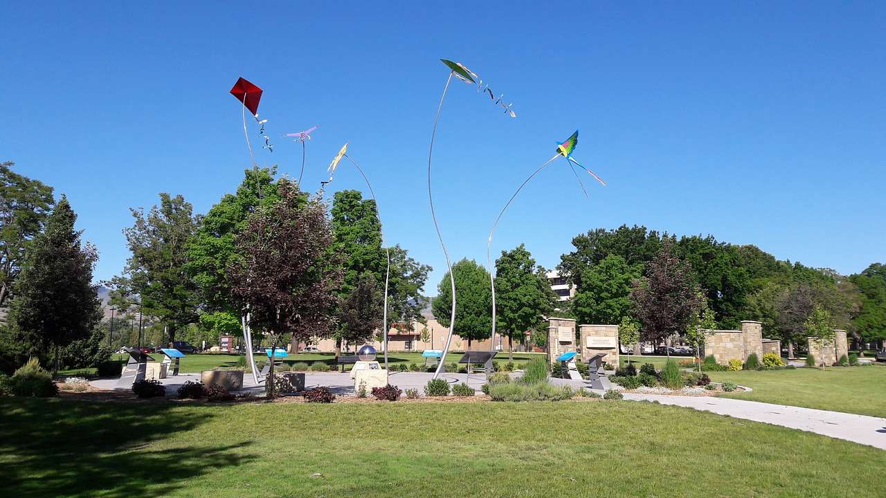 A park with green grass, trees, and a sculpture of flying kites