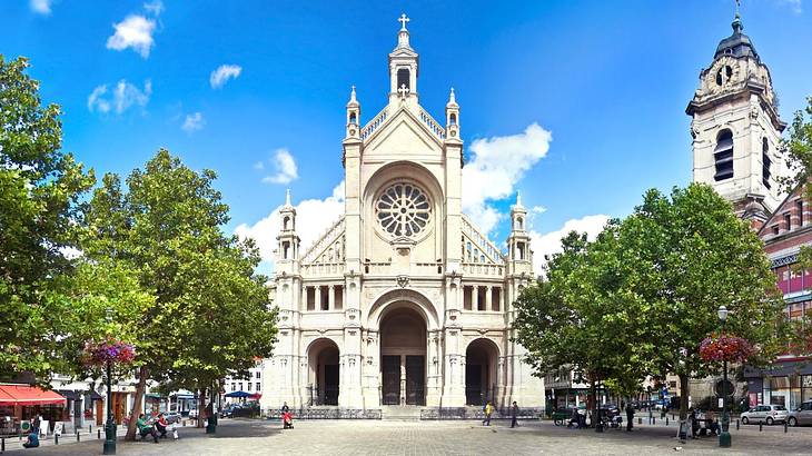 A white French Gothic church with trees outside and a square in front of it