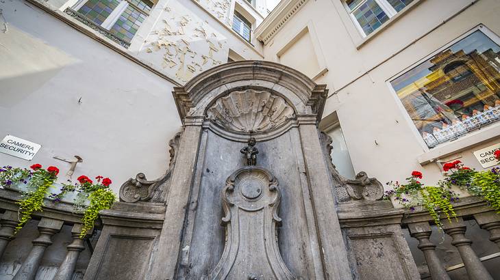 A small bronze sculpture of a boy urinating against white buildings