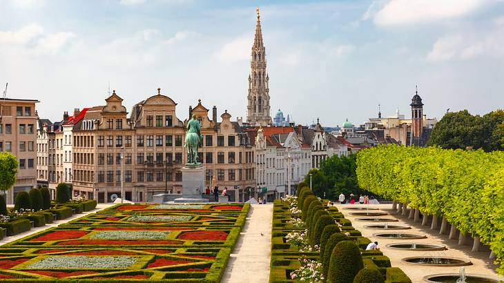 A garden with colorful flowers and trees and historical buildings behind it