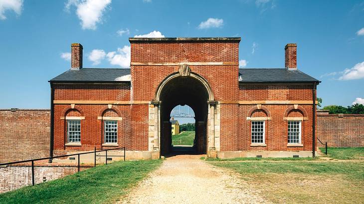A red-brick fort building with an arched opening under a partly cloudy sky