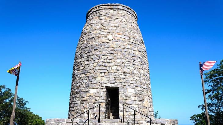 An old stone tower with a flag on each side under a clear blue sky