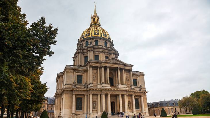 A museum building with a dome on top and people in front under a cloudy sky