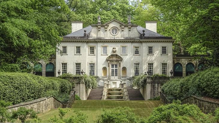 A stone manor house with steps and a garden in front of it and trees surrounding it