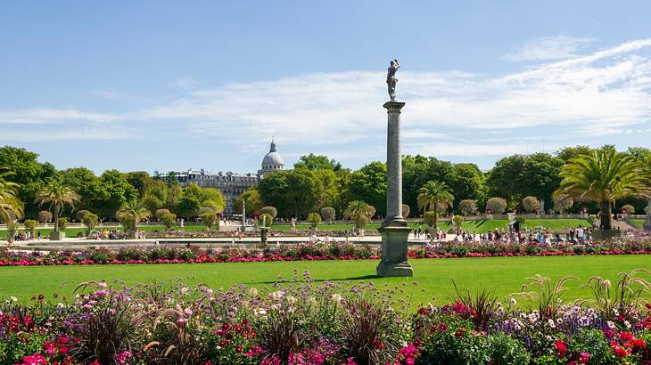 Landscape view of a colourful garden with flowers, trees, and monument on a sunny day