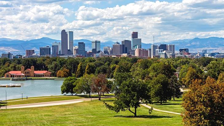 A park with green grass, trees, and a lake and a city skyline in the distance