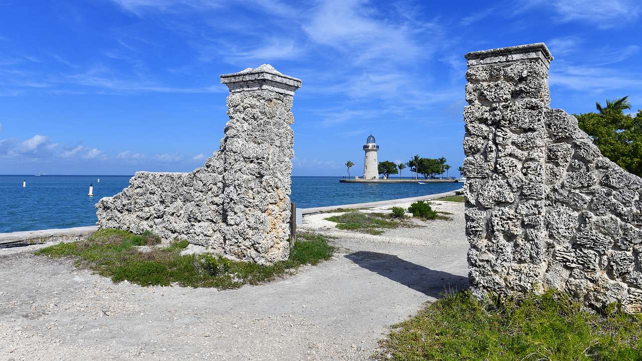 A stone-made entrance on a beach with blue water and a watch tower in the background