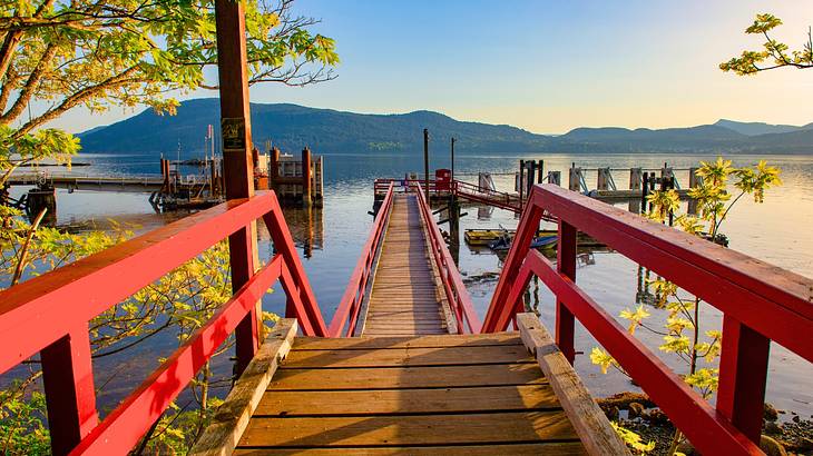 A red steel and wood ferry dock surrounded by the sea and mountains in the background