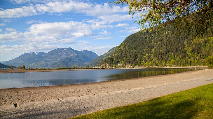 A serene lake under a partly cloudy sky with green mountains in the background