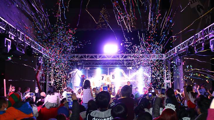 People partying under neon lights looking forward towards a brightly lit stage