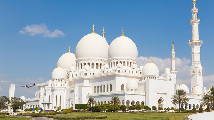 Large white mosque with a flying plane on the left and a vast green courtyard