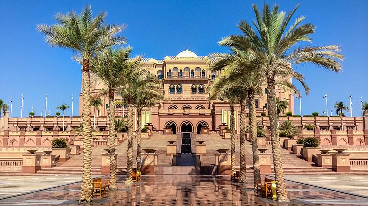 Front view of a grand palace hotel surrounded by green palm trees against a blue sky