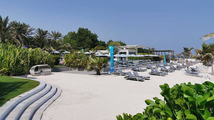 A broad view of a beach resort with umbrellas, chairs, greenery, and white sand