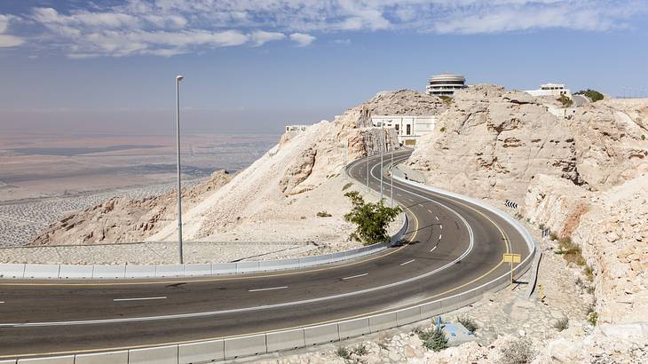 Winding road to a mountain peak with a steel post on the left under the blue sky