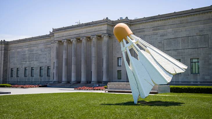 A giant sculpture of a shuttlecock in front of a concrete building with pillars