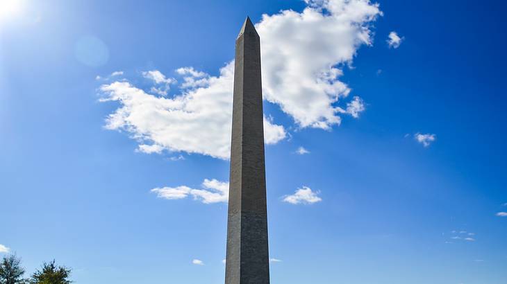 A tall obelisk surrounded with flags at its bottom on a sunny day