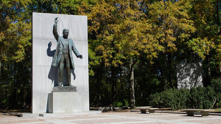 A life-sized statue of a man with a raised hand surrounded by trees
