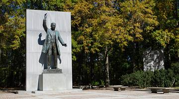 A life-sized statue of a man with a raised hand surrounded by trees