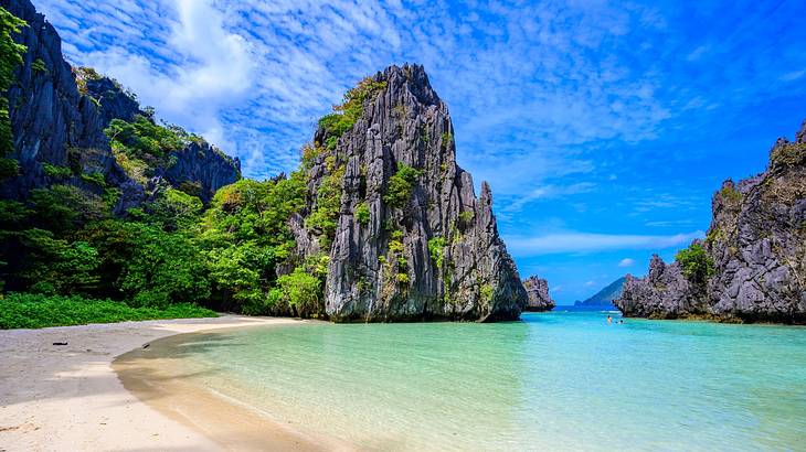 A rocky cliff with greenery next to white sand and turquoise water