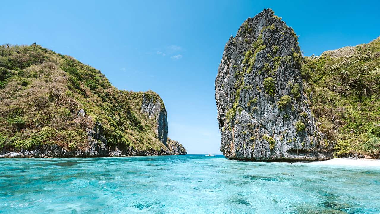 A rocky island surrounded by clear blue water and blue skies