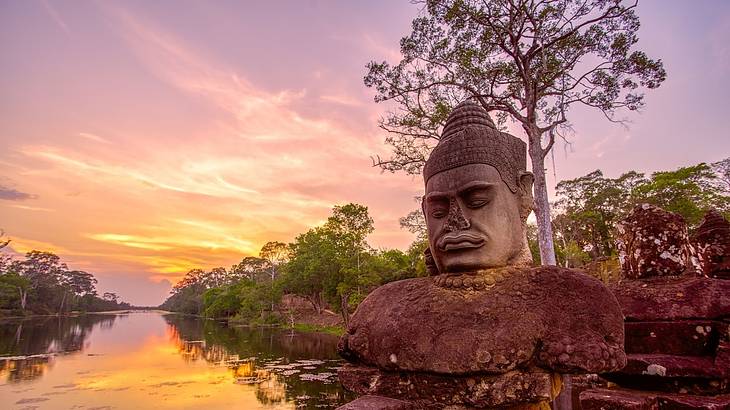 A beautiful landscape of an ancient buddha head statue along water with trees