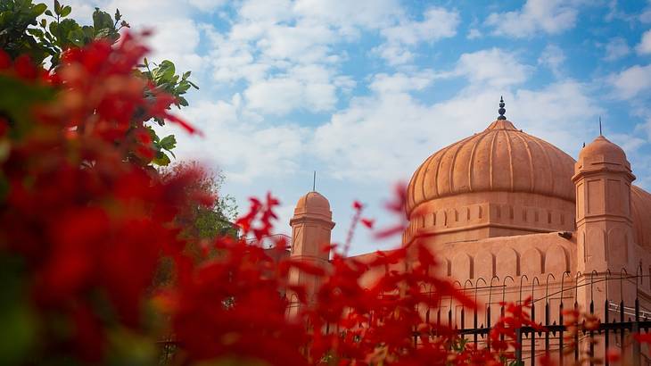 The outside architecture of a beautiful fort, behind a red bush, on a nice day