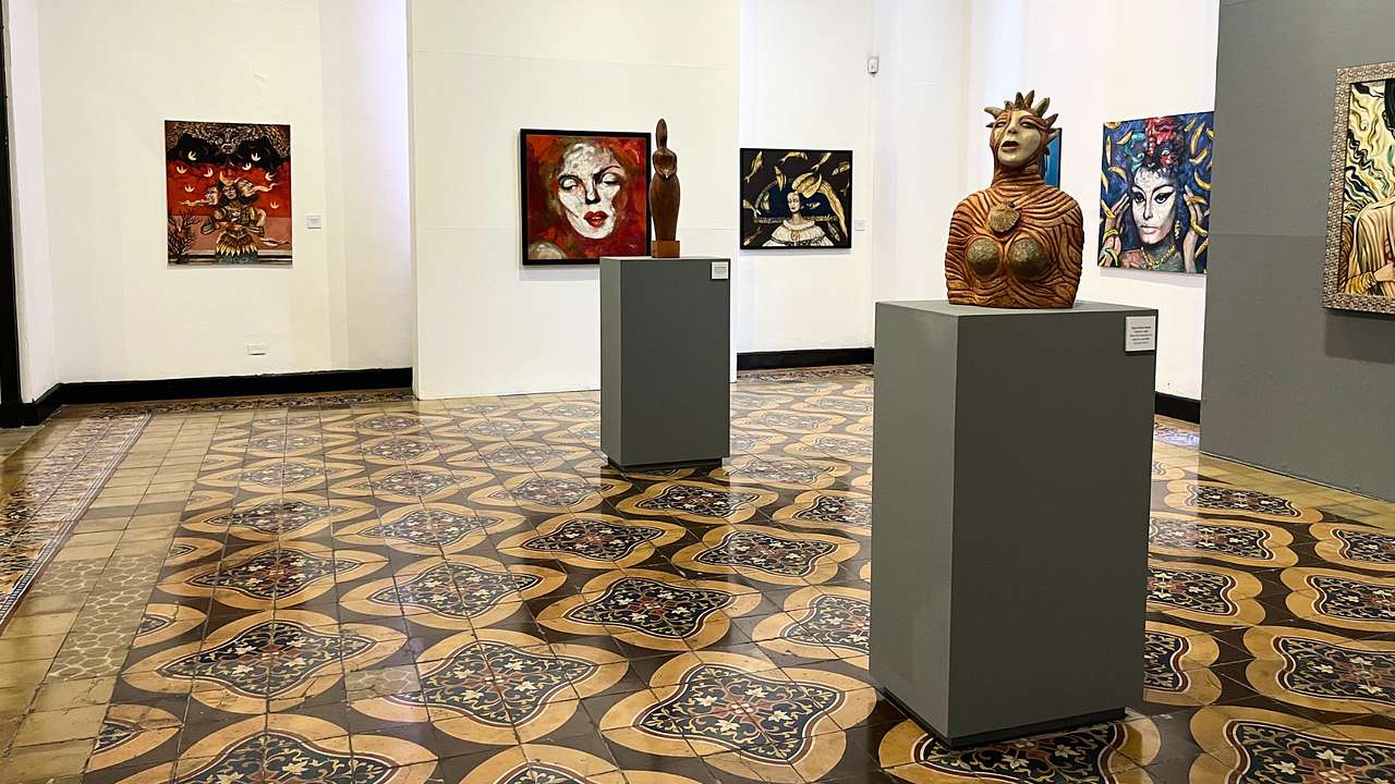 Inside an art exhibit room with paintings on the walls and two sculptures on stands