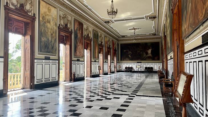 The inside of a grand ballroom with a checkered floor and paintings on the walls
