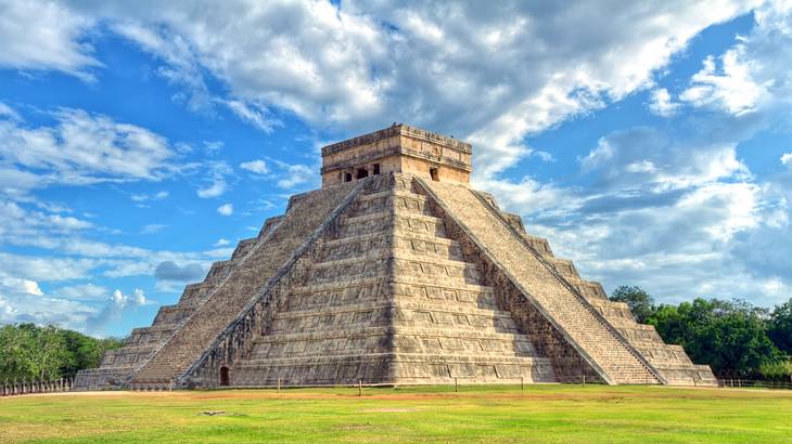 A stone pyramid on the grass under a blue sky with clouds