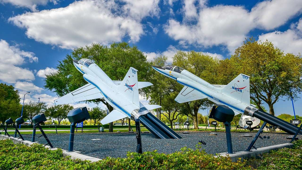 Two white and blue planes with NASA logos surrounded by greenery