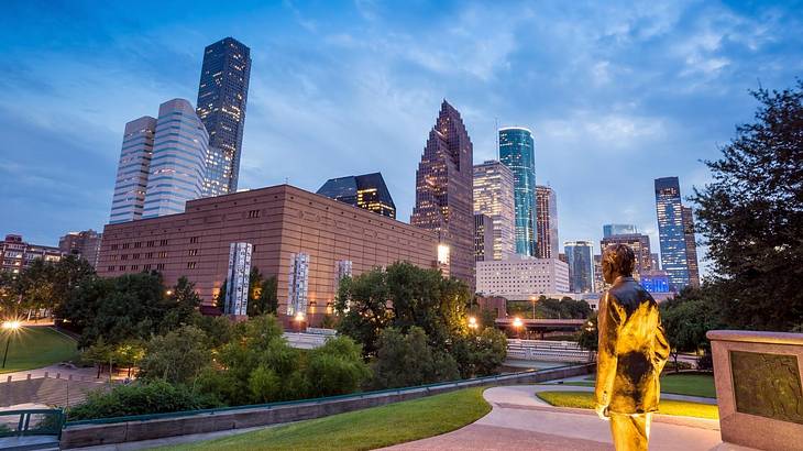 A skyline illuminated at night with a statue of a person in the foreground