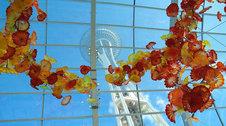 Red, orange, and yellow glass flowers in front of a window and an observation tower