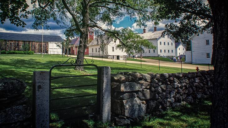 View of a village with wooden cottages from outside a stone fence and metal gate