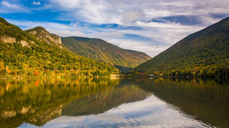 A lake at the bottom of lush mountains on a partly cloudy day