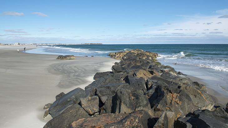 Massive rock boulders piled up in a line on a sandy shore