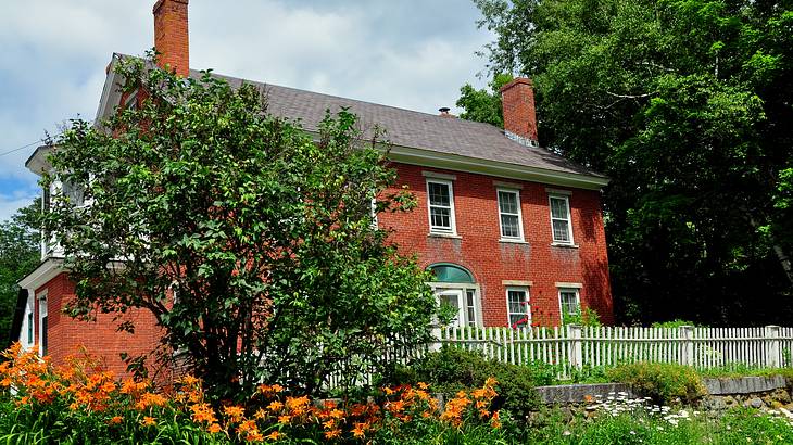 A 2-story red brick house with a garden and white fence in front