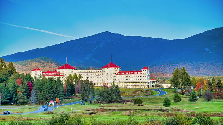 A white palace-like building with a red roof, surrounded by greenery and a mountain