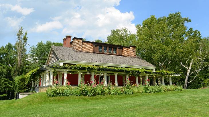 A house with columns, surrounded by plants and trees, and a green lawn in front