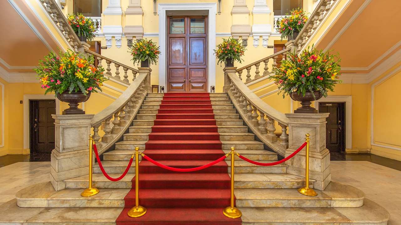 A set of stairs with a red runner and flowers on the banister in a grand building