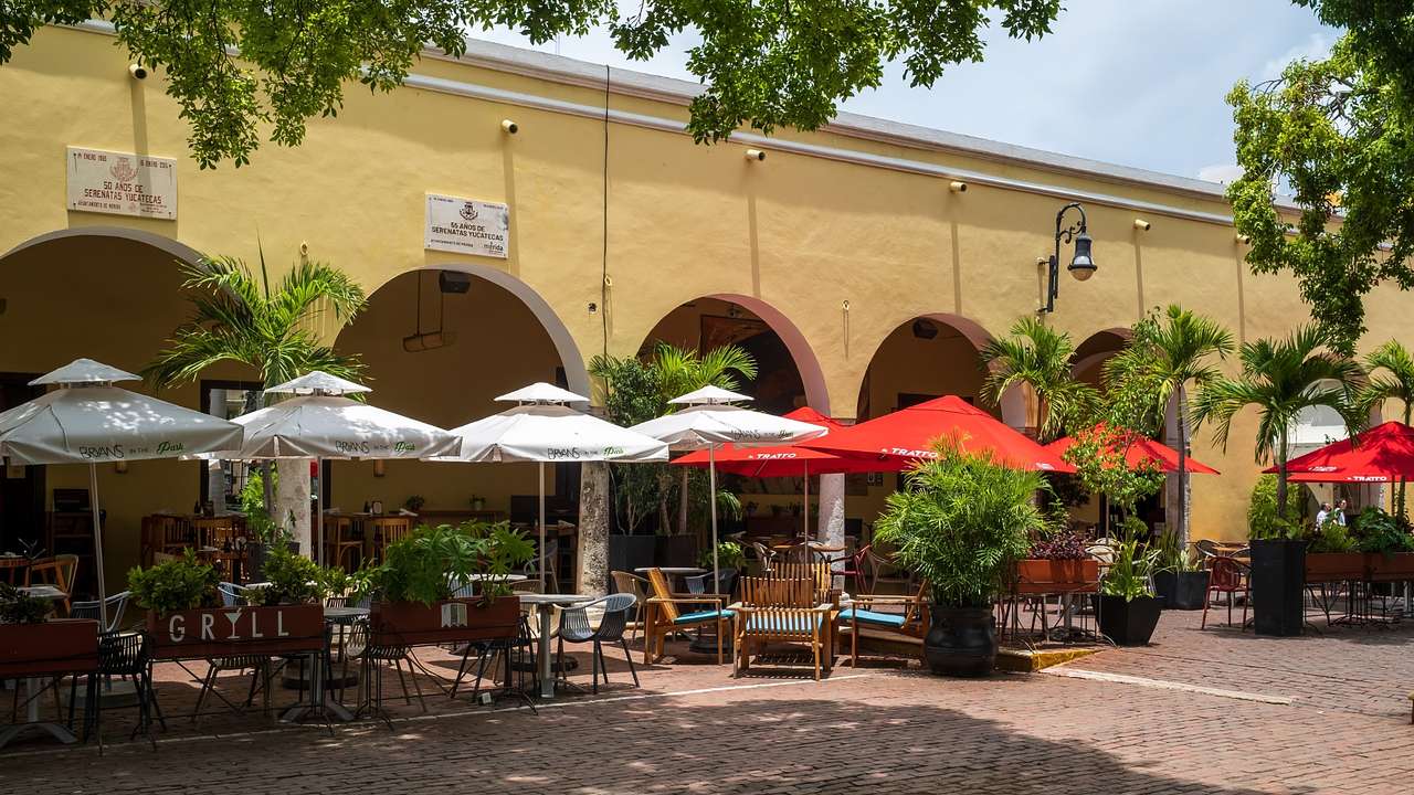 A patio with tables and sun umbrellas next to a yellow building and trees