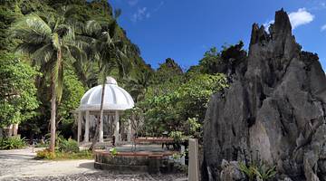 A white shrine surrounded by green trees and a tall rock on an island, Palawan