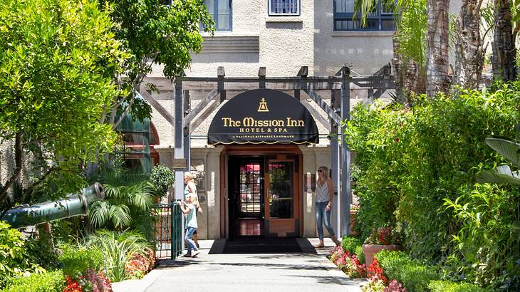 The front of a hotel with a "Mission Inn Hotel & Spa" sign next to plants and a path